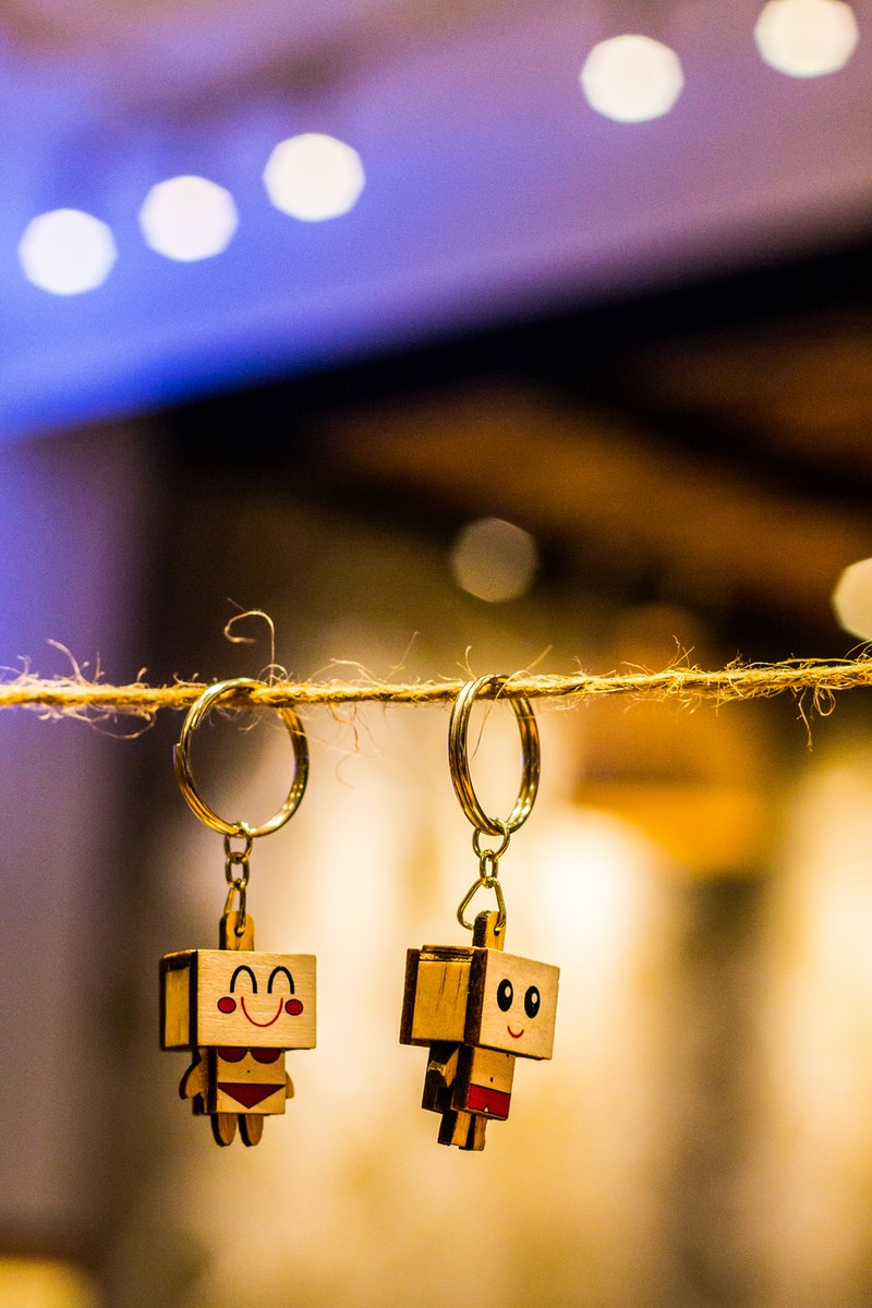 Bokeh Photography of Two Wood Block Man and Woman Figure Key Chains Hanging on Brown Thread